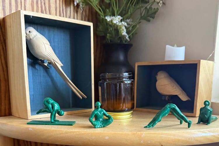 A corner shelf holding two carved birds in frames and small green toy soldiers posed in yoga positions